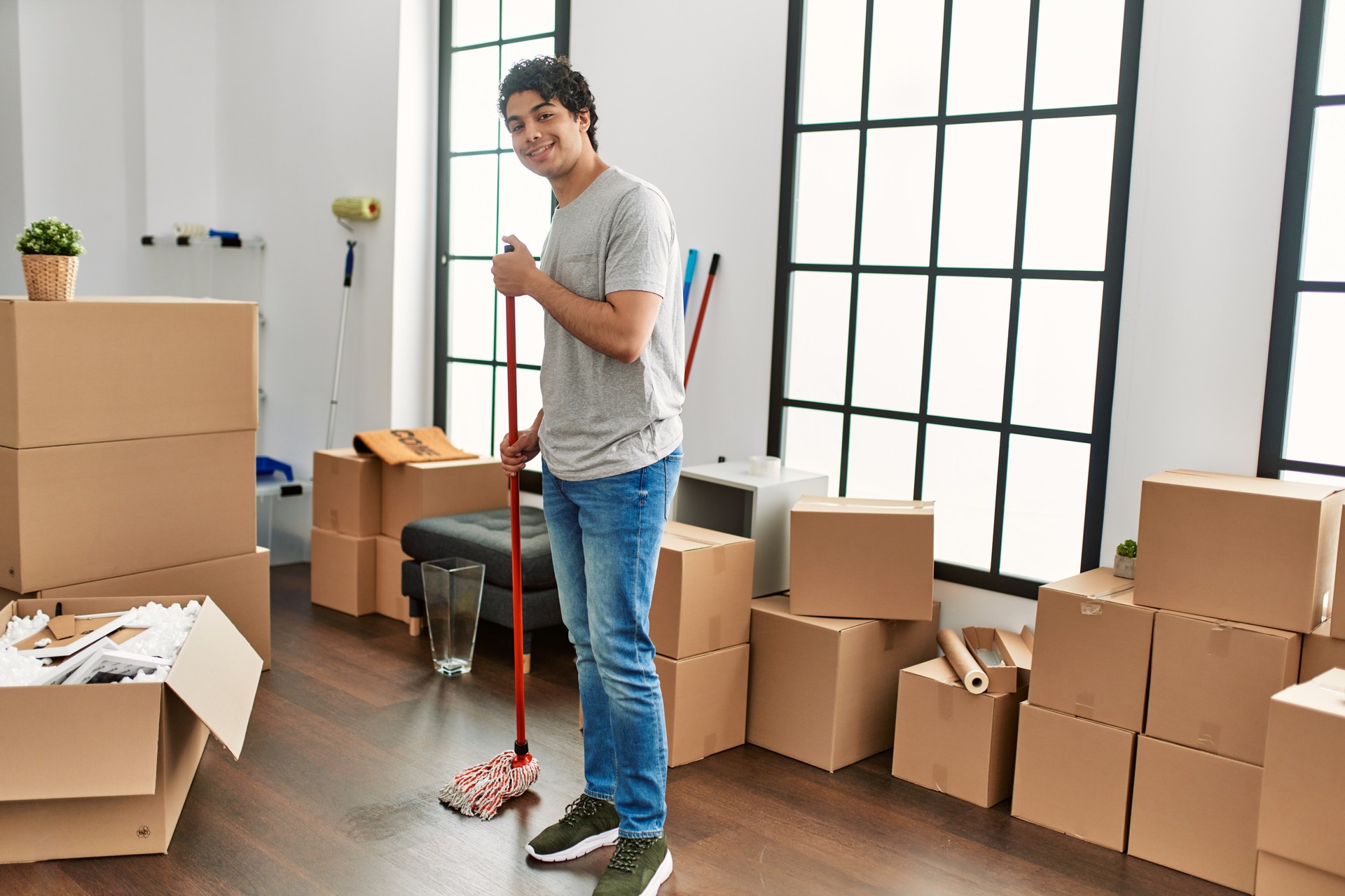 Young hispanic man smiling happy cleaning floor at new home.